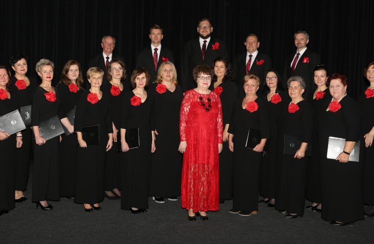 Na zdjęciu członkowie chóru mieszanego Cantabile z Zagórowa. Panie w długich czarnych sukniach z wpiętymi czerwonymi różami w pierwszym rzędzie. W drugim - panowie z różami w klapach czarnych marynarek. Pośród pań na środku stoi dyrygentka w czerwonej koronkowej sukni