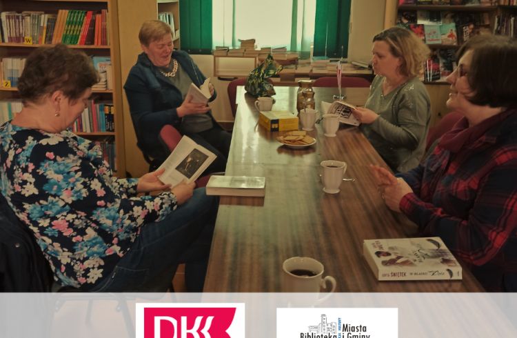 Na zdjęciu cztery panie czytające książkę, siedzące wspólnie przy stoliku.