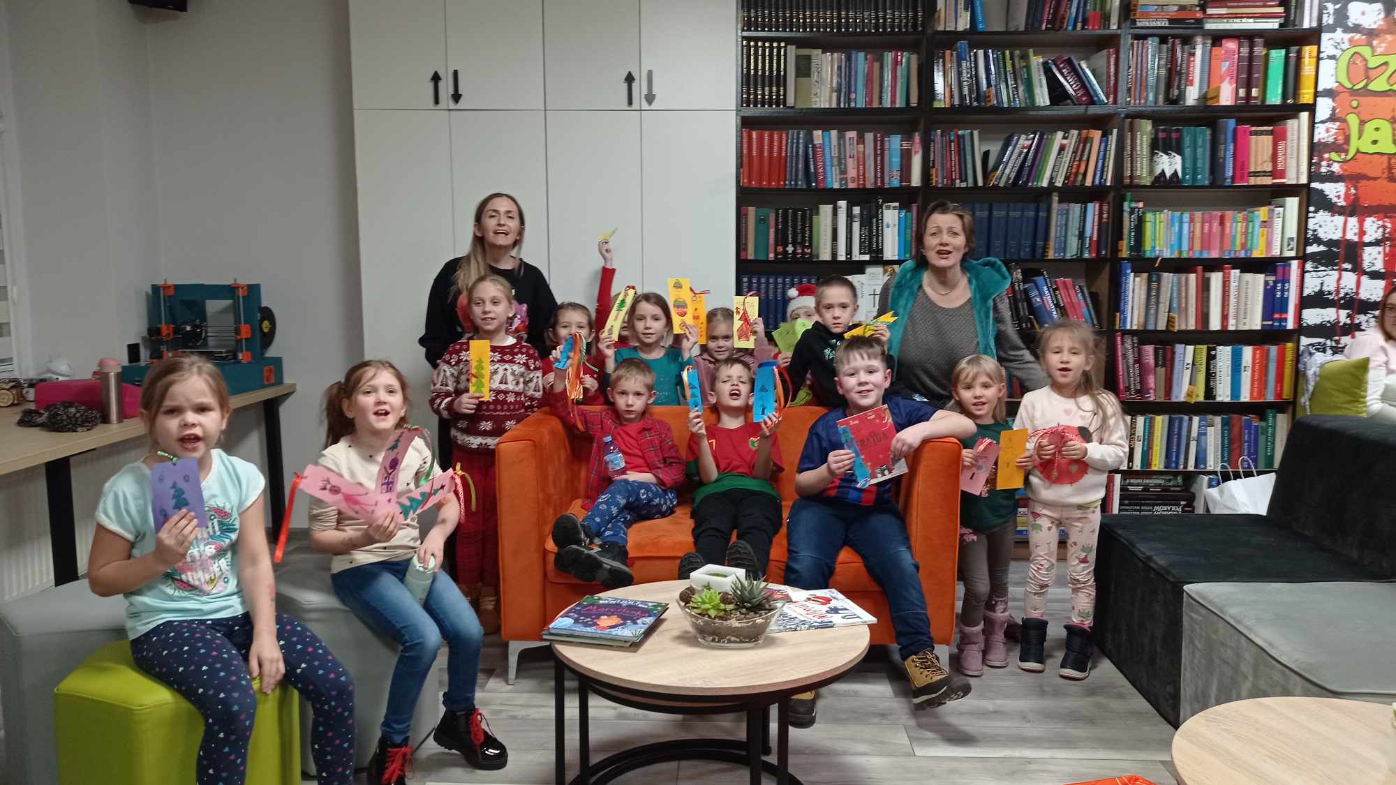 Grupa dzieci z bibliotekarkami pozuje do zdjęcia, trzymając w ręku zakładki do książek