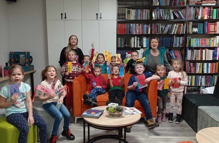 Grupa dzieci z bibliotekarkami pozuje do zdjęcia, trzymając w ręku zakładki do książek